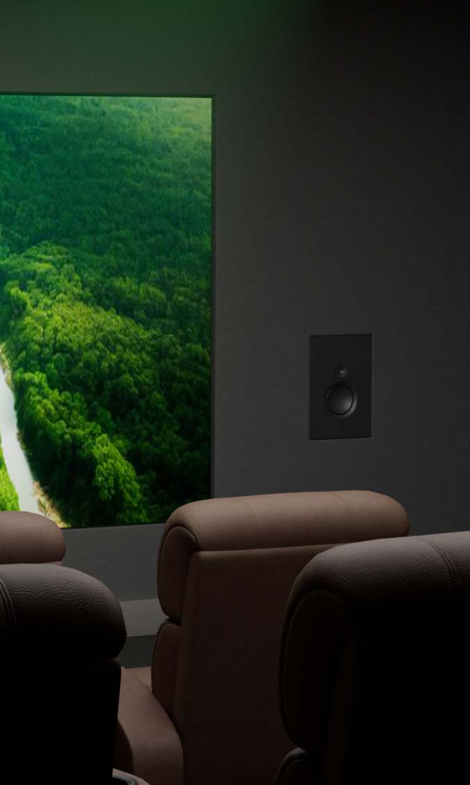 In-wall home theater speaker mounted next to a screen showing a forest landscape