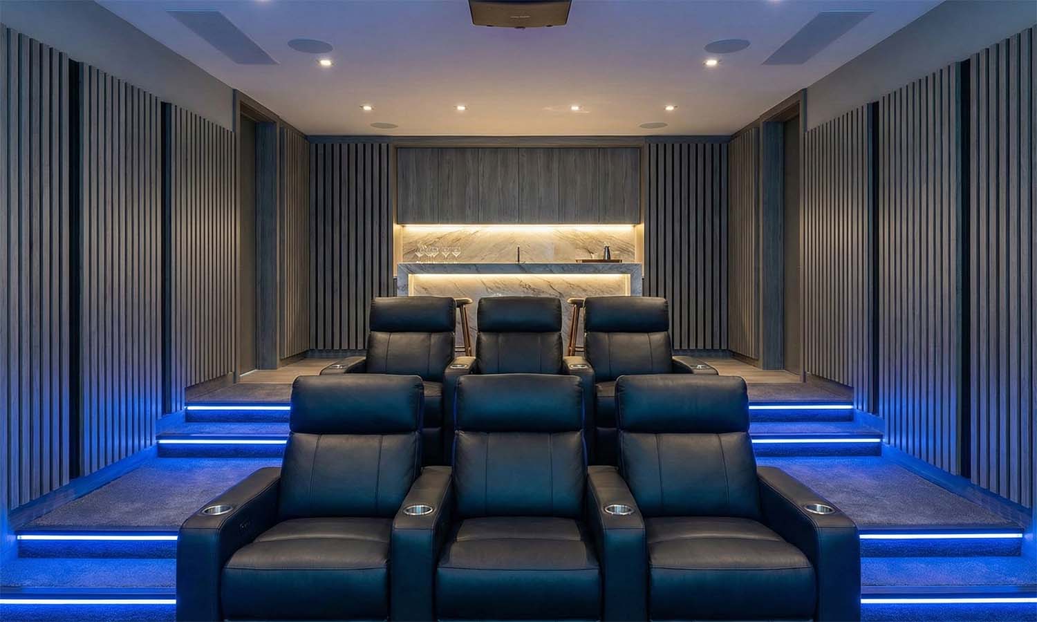 Home theater room with two tiers of black leather seating and a backlit bar in the back