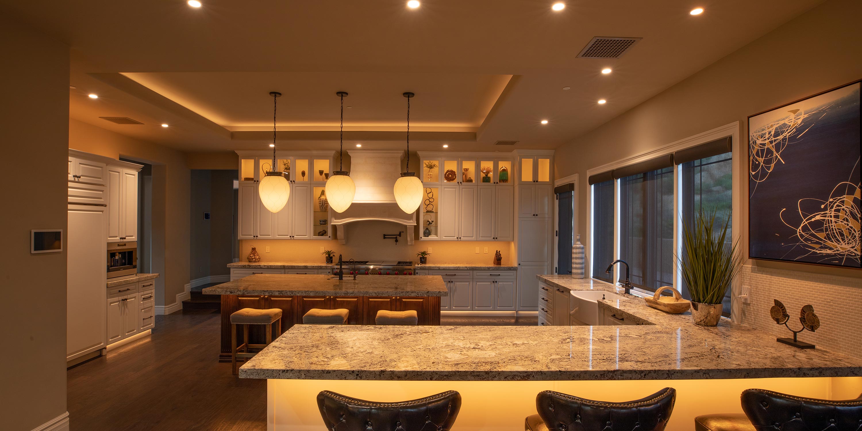 Elegant kitchen featuring granite islands, pendant lighting, and illuminated cabinets