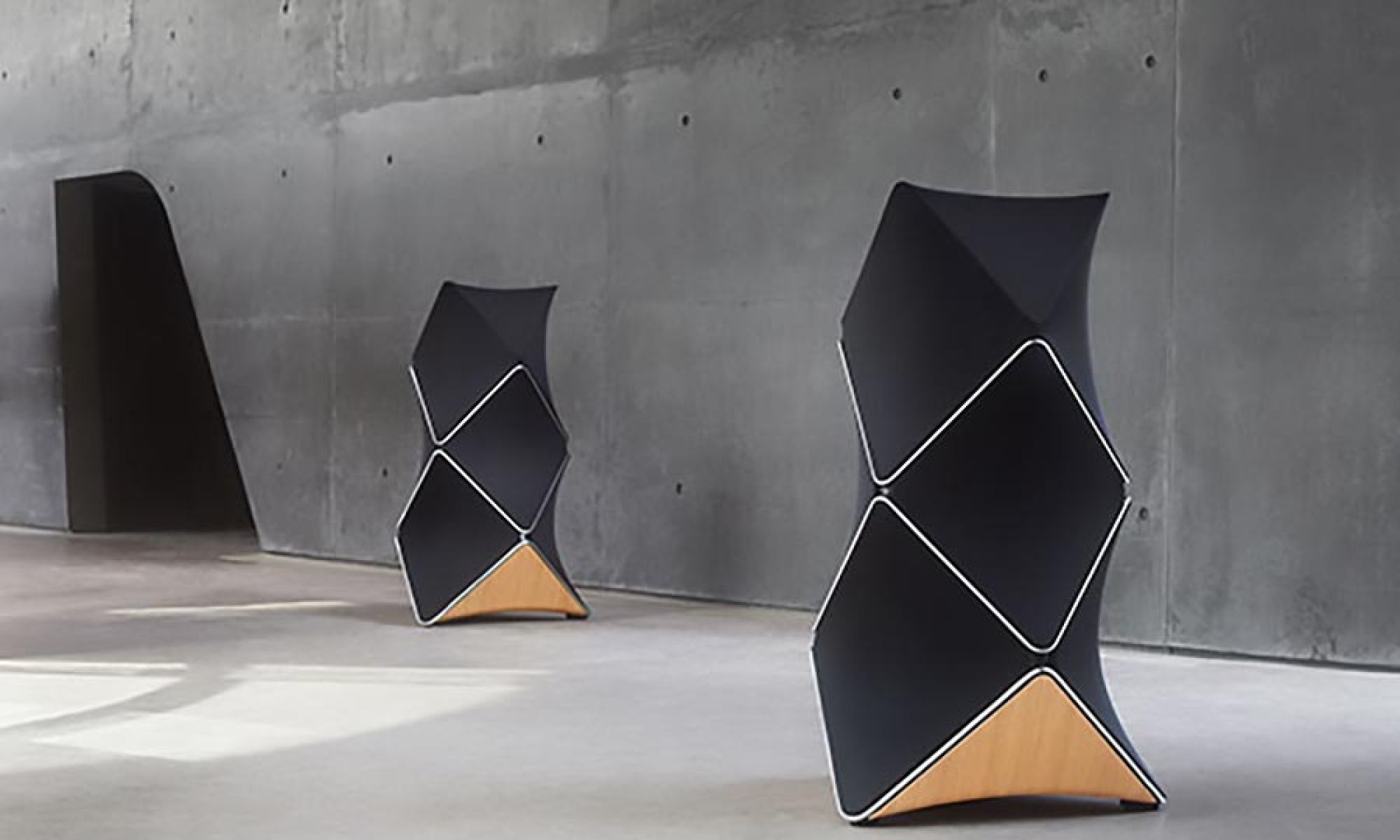 Two modern geometric black and wood floor speakers in a minimalist concrete room