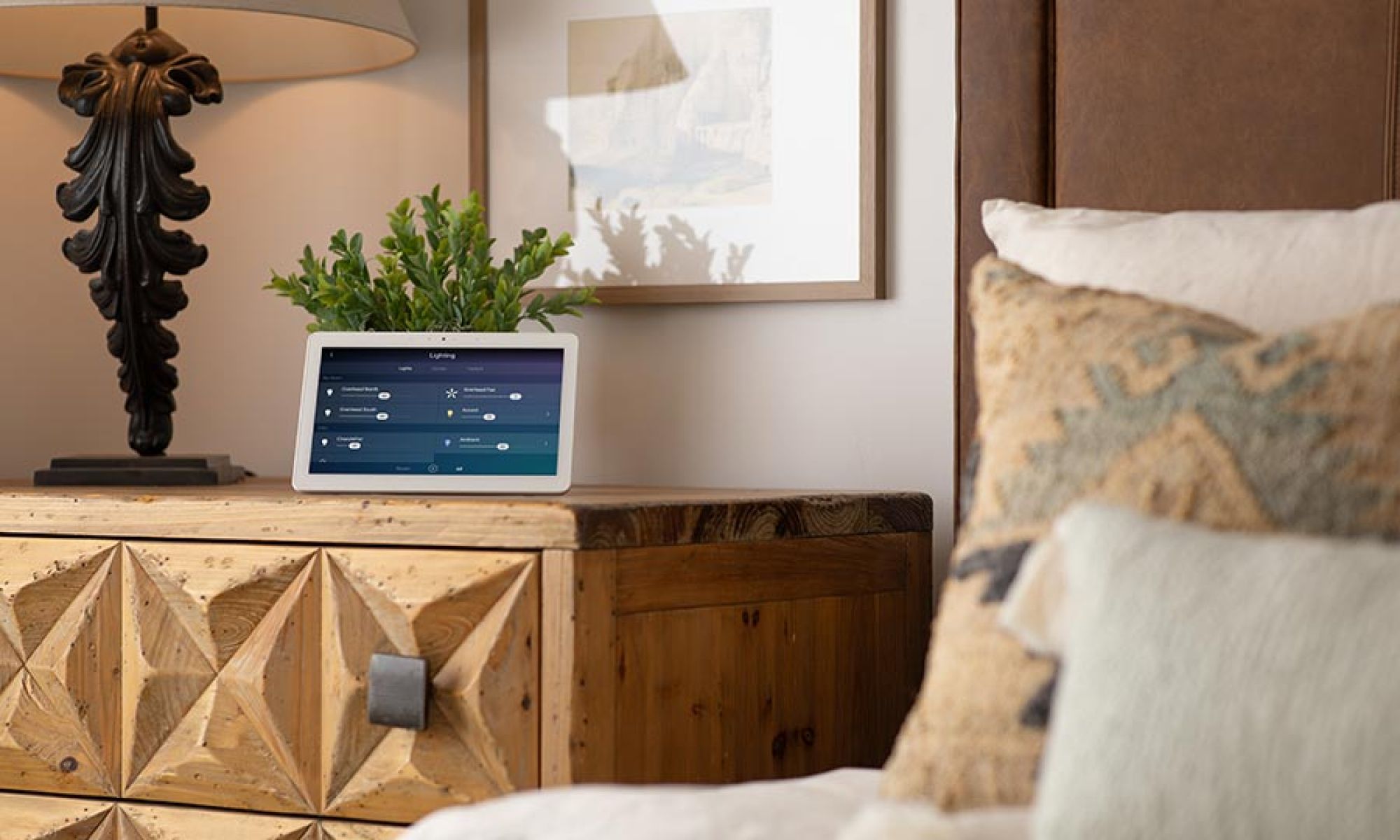 Smart home control tablet on a wooden nightstand next to a bed