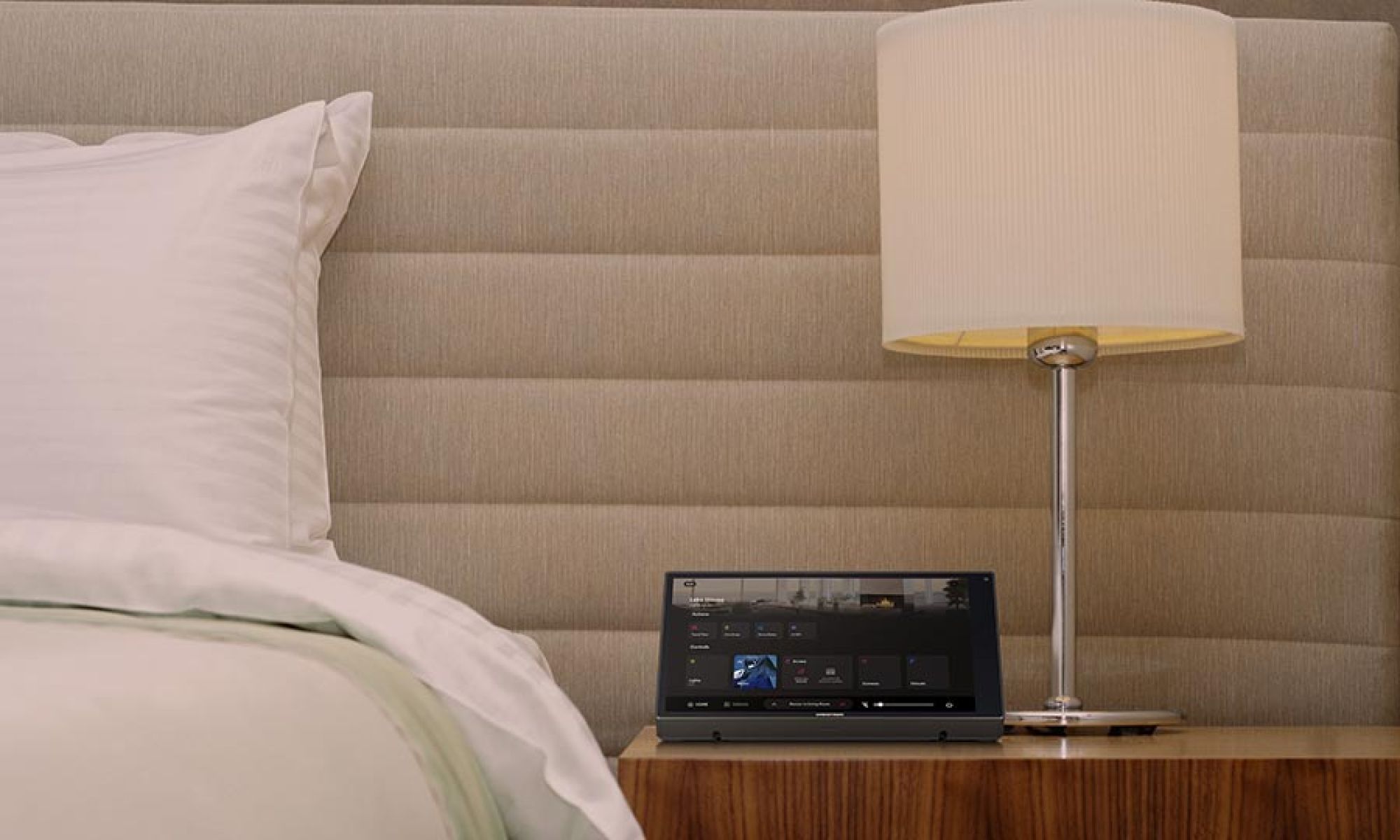 Touchscreen control panel on a wooden nightstand next to a bed and lamp